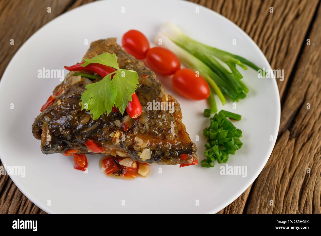 Frittierte Fischköpfe mit Chili auf einem weißen Teller mit Tomaten und Frühlingszwiebeln. Stockfoto