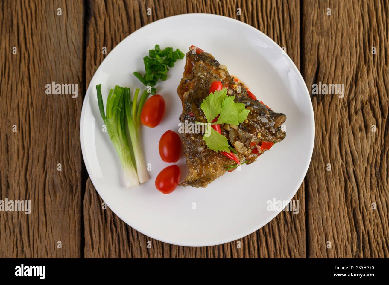 Frittierte Fischköpfe mit Chili auf einem weißen Teller mit Tomaten und Frühlingszwiebeln. Stockfoto