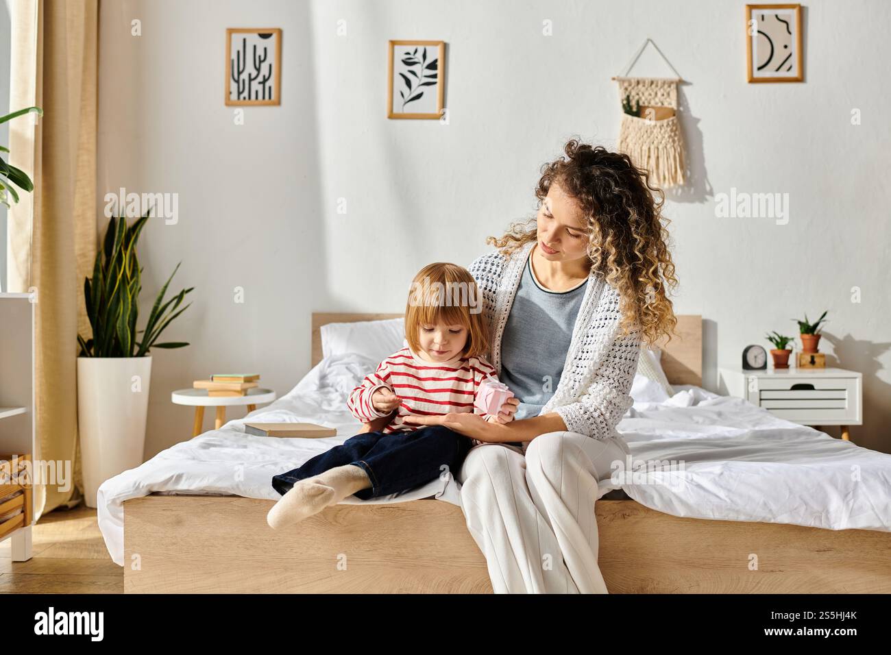 Mutter und Tochter mit lockigen Haaren teilen besondere Momente auf einem stilvollen Bett und pflegen ihre Bindung. Stockfoto