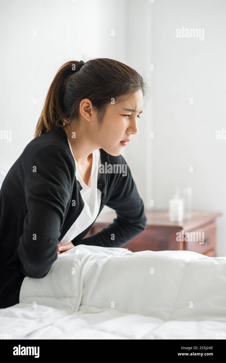 Eine Frau, die mit Bauchschmerzen im Bett sitzt und ihre Hand auf den Bauch drückt. Stockfoto