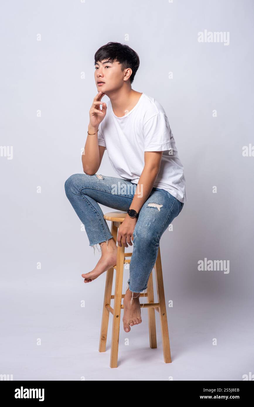 Ein junger Mann in einem weißen T-Shirt sitzt auf einem Hochstuhl. Stockfoto Ein junger Mann in einem weißen T-Shirt sitzt auf einem Hochstuhl. Stockfoto