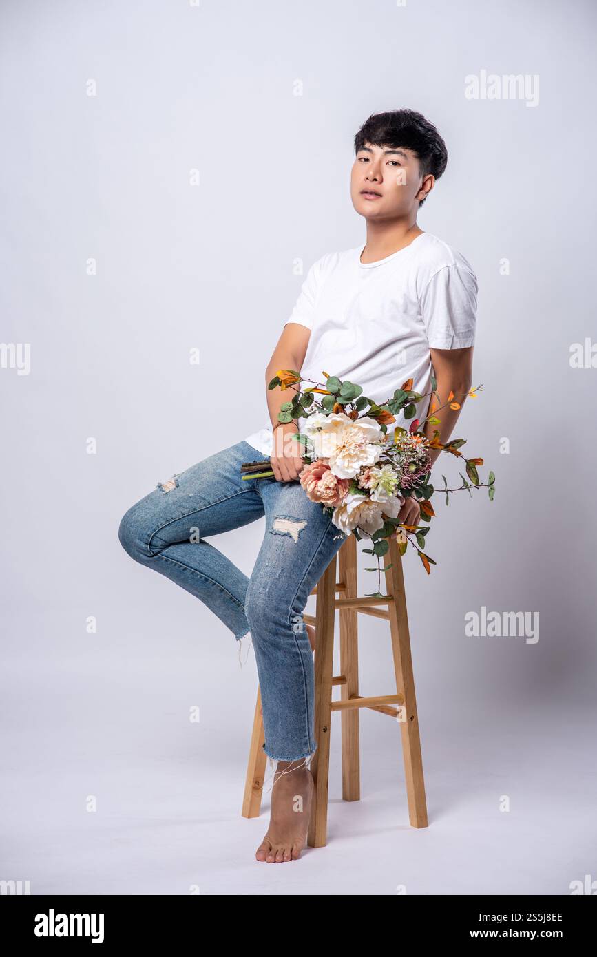 Ein junger Mann in einem weißen T-Shirt sitzt auf einem Hochstuhl und hält Blumen. Stockfoto Ein junger Mann in einem weißen T-Shirt sitzt auf einem Hochstuhl und hält Blumen. Stockfoto