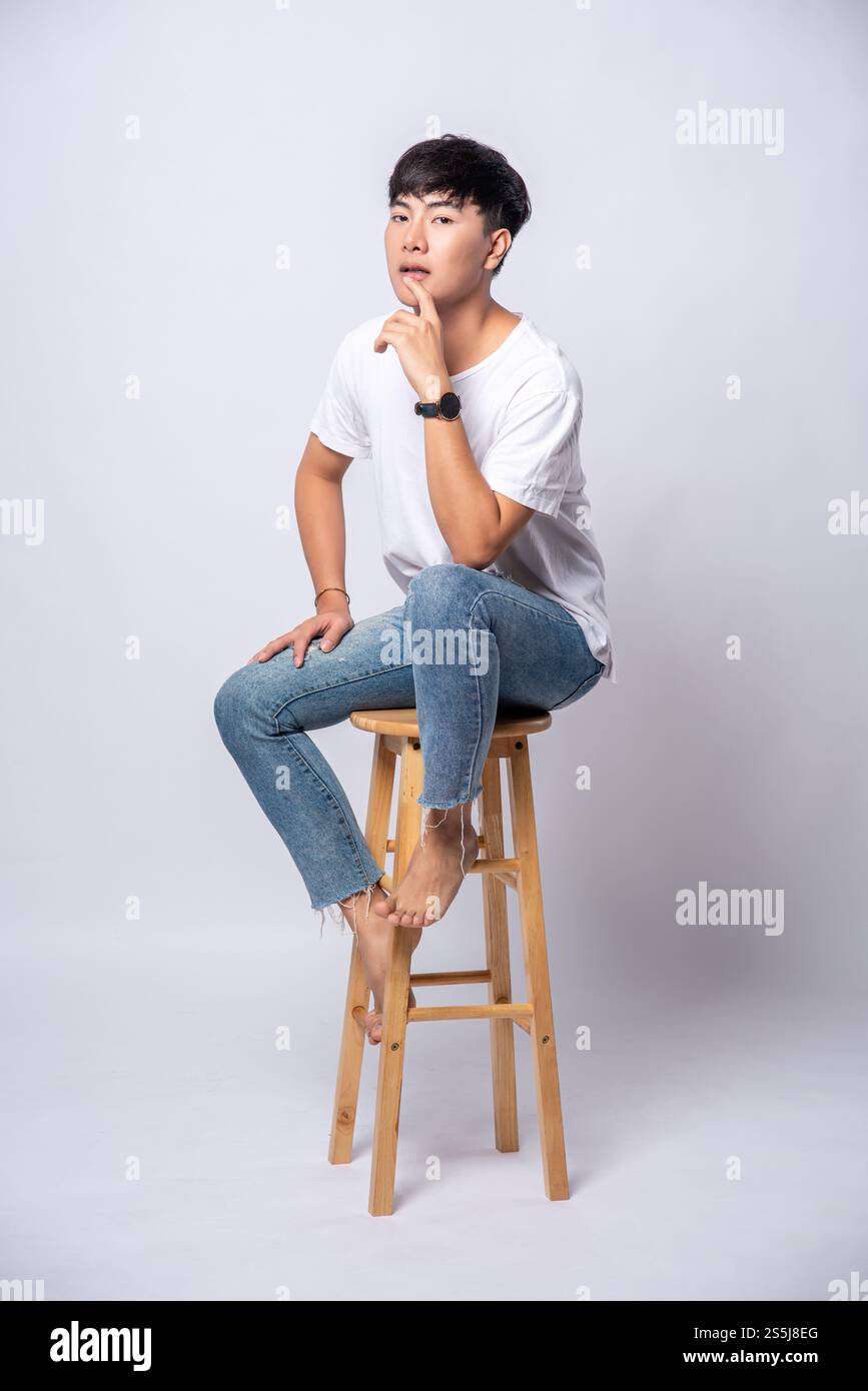 Ein junger Mann in einem weißen T-Shirt sitzt auf einem Hochstuhl. Stockfoto Ein junger Mann in einem weißen T-Shirt sitzt auf einem Hochstuhl. Stockfoto