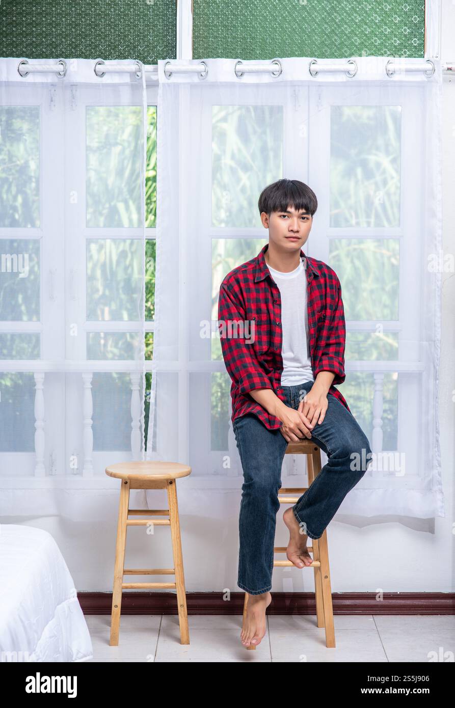 Ein junger Mann in einem gestreiften Hemd sitzt auf einem Hochstuhl. Stockfoto Ein junger Mann in einem gestreiften Hemd sitzt auf einem Hochstuhl. Stockfoto