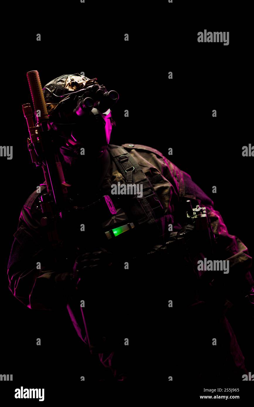 Ein taktischer Operator, der Kampfausrüstung trägt und mit einer Nachtsichtbrille in dunkler Umgebung ausgestattet ist und die militärische Vorbereitung in einem visuellen Striki darstellt Stockfoto