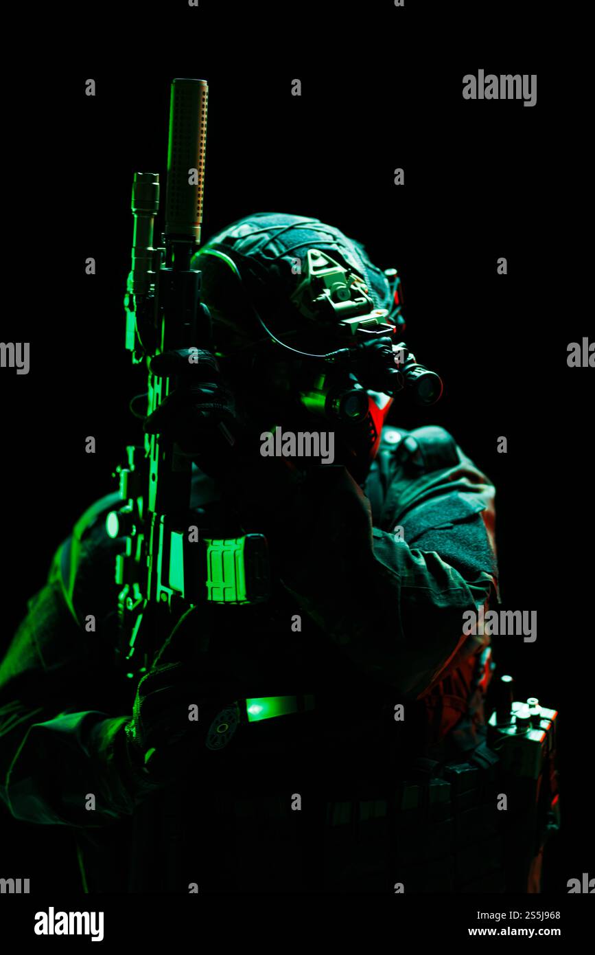 Ein Soldat mit fortschrittlicher taktischer Ausrüstung, einschließlich Nachtsichtbrille, beleuchtet von grünem Licht, steht vor dunklem Hintergrund und hält einen Stockfoto