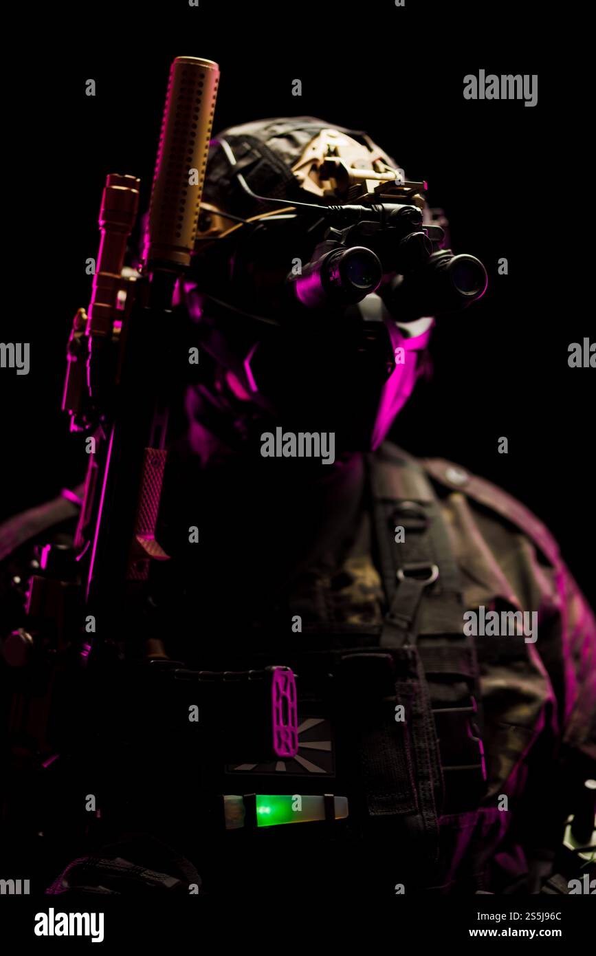 Ein Soldat in taktischer Ausrüstung und Nachtsichtbrille wird von rosa und grünem Licht beleuchtet, was High-Tech-Operationen und Einsatzbereitschaft symbolisiert. Perfekt Stockfoto