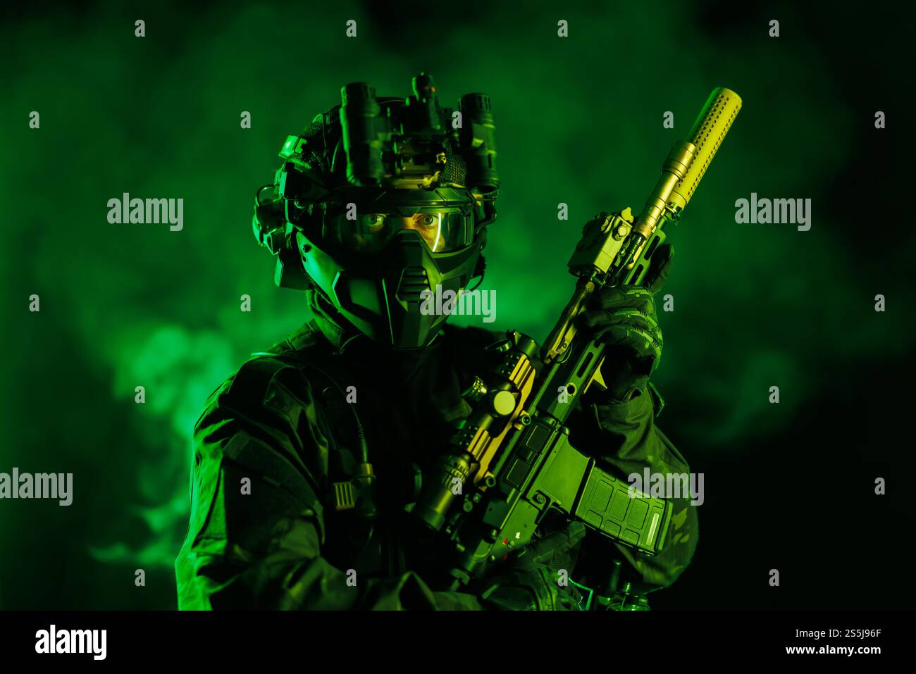 Ein Soldat, ausgestattet mit taktischer Ausrüstung und Nachtsichttechnologie, hält ein fortschrittliches Gewehr vor einem grünen rauchigen Hintergrund. Intensiv und Kino Stockfoto