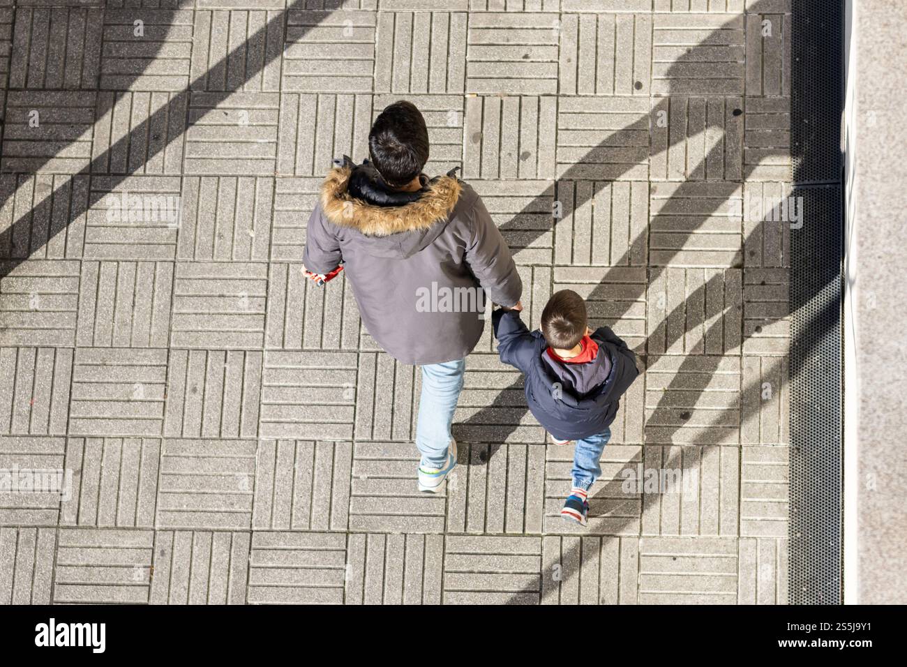 Vater und Sohn halten Hände, die auf einem Bürgersteig laufen, von oben gesehen Stockfoto
