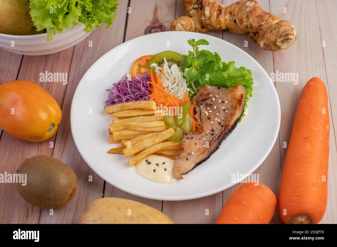 Fischsteak mit Pommes frites, Kiwi, Salat, Karotten, Tomaten, und Kohl in einer weißen Schale. Stockfoto
