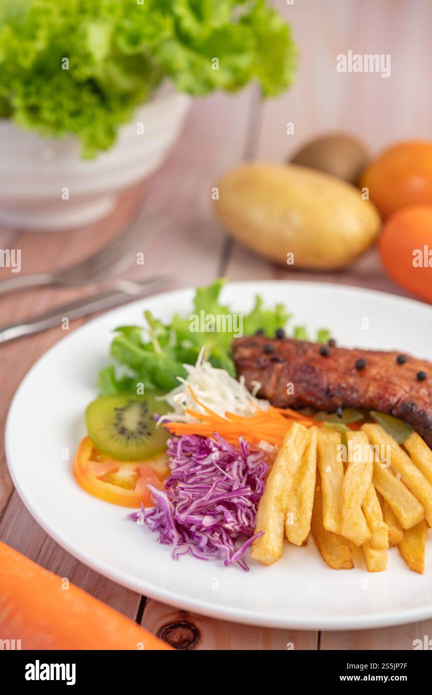 Fischsteak mit Pommes frites, Kiwi, Salat, Karotten, Tomaten, und Kohl in einer weißen Schale Stockfoto