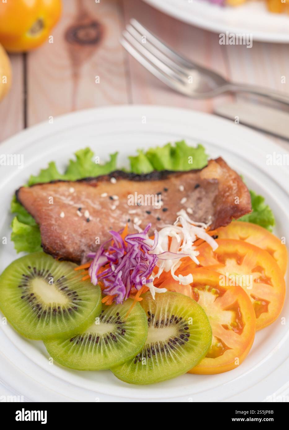Fischsteak mit Pommes frites, Kiwi, Salat, Karotten, Tomaten, und Kohl in einer weißen Schale Stockfoto