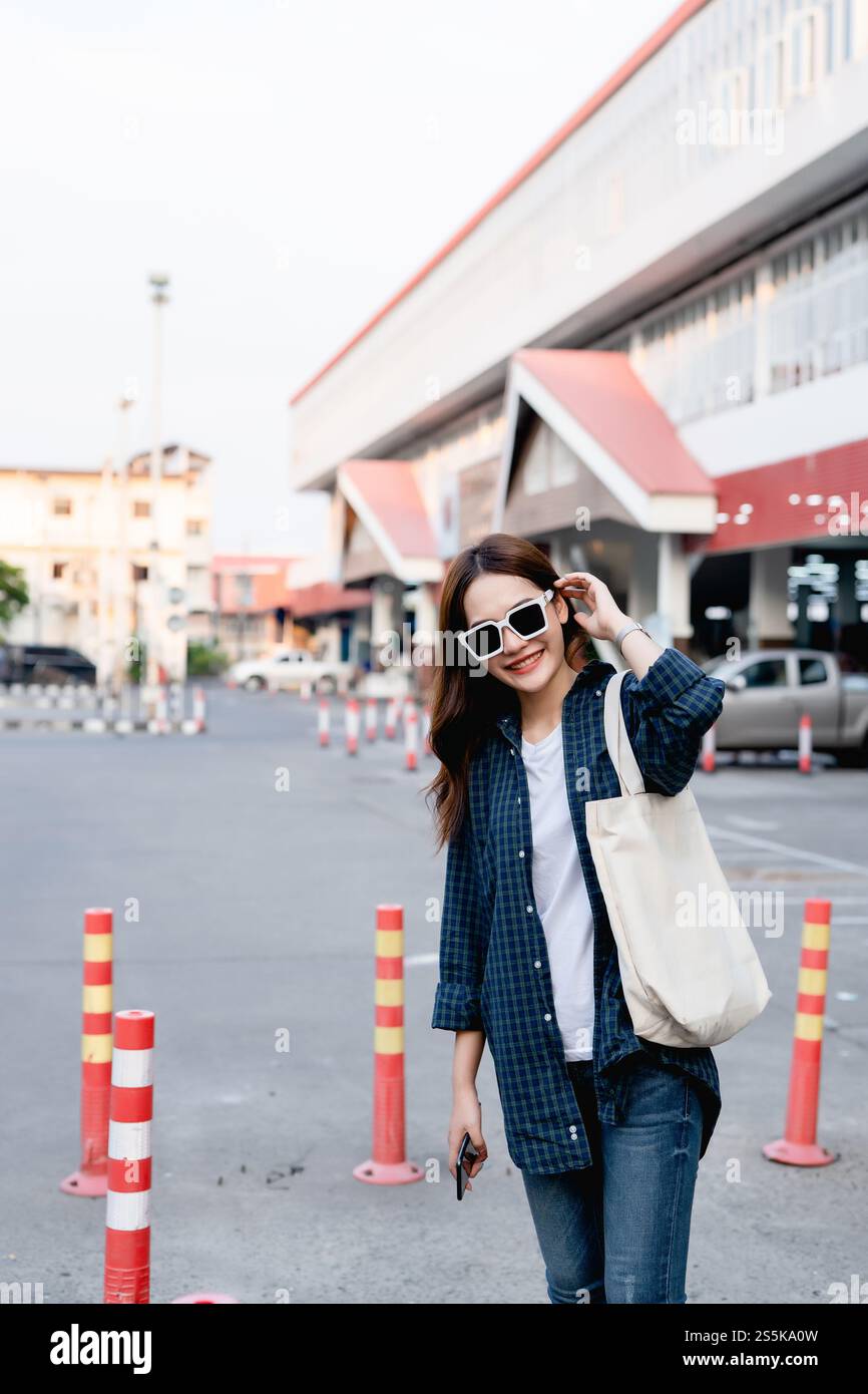 Porträt hübsche Frau in Sonnenbrille mit einer großen Tasche auf der Schulter stehend mit Blick auf Kamera und Lächeln, Junge Touristen halten Handy in der Hand Stockfoto