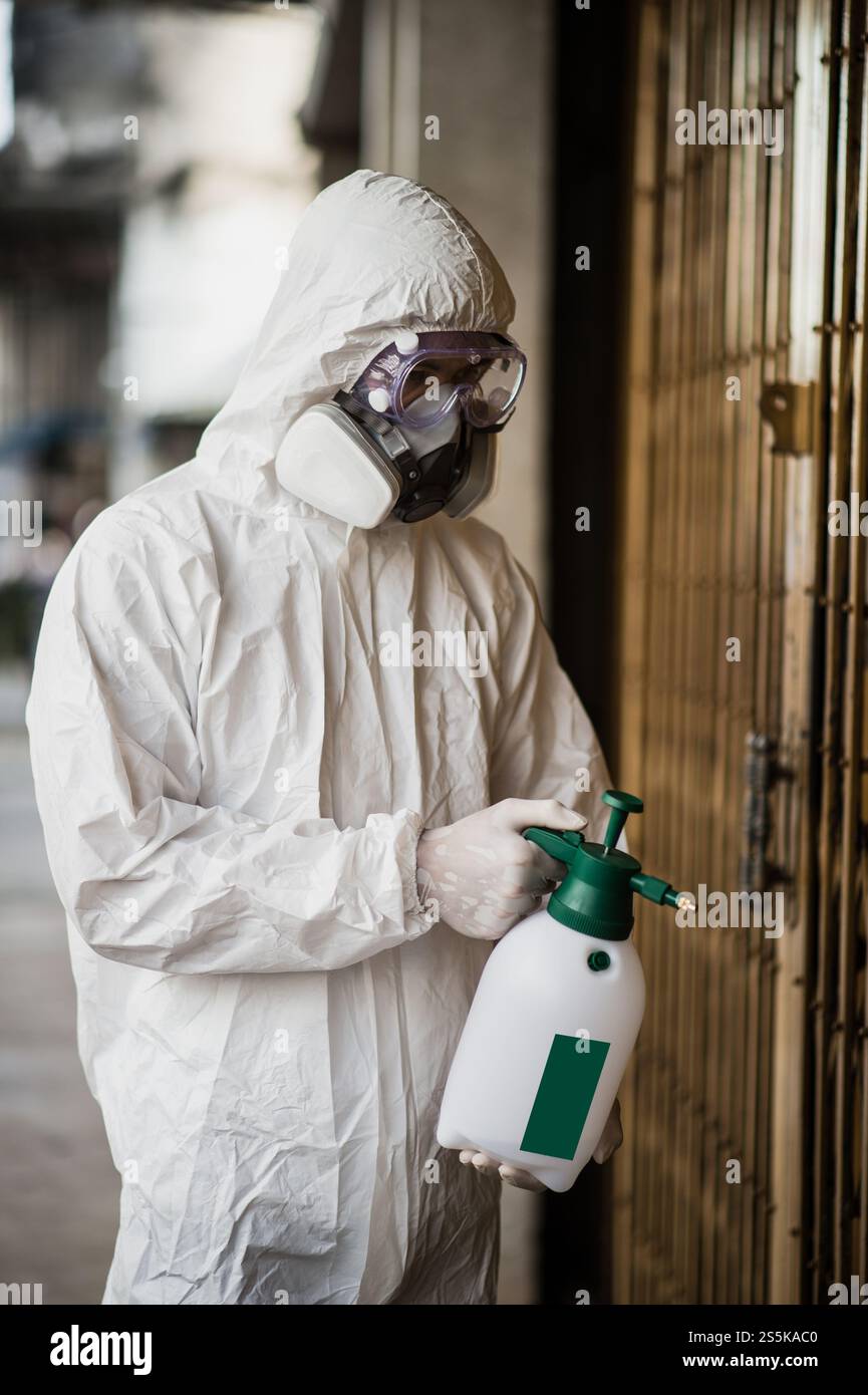Desinfektionsspezialist Mann trägt persönliche Schutzausrüstung (psa) Anzug, Handschuhe, Maske und klare Brille, reinigt Straßen mit einer Flasche Stockfoto