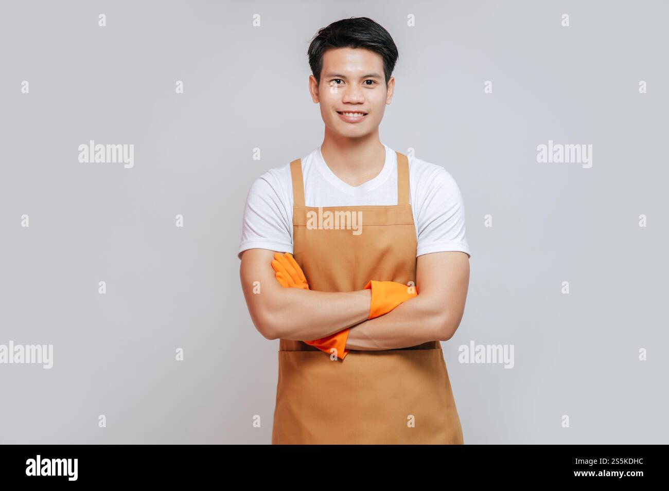 Porträt Asiatische junge, gutaussehende Mand steht mit überkreuzten Armen, er trägt Schürze und Gummihandschuhe, lächelt und blickt in die Kamera, Kopierraum Stockfoto