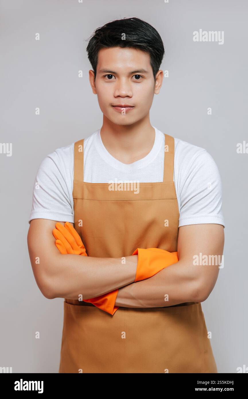 Porträt Asiatische junge, gutaussehende Mand steht mit überkreuzten Armen, er trägt Schürze und Gummihandschuhe, lächelt und blickt in die Kamera, Kopierraum Stockfoto