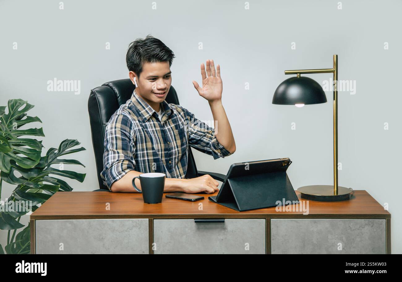 Glücklich junger gutaussehender Mann mit neuer Normal, bleibt zu Hause und arbeitet von zu Hause aus auf einem digitalen Tablet und verwendet Smartphone während der Selbstisolierung und Stockfoto