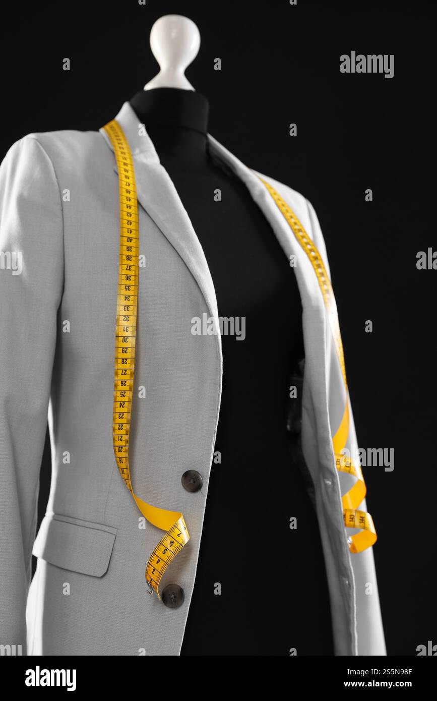 Weibliche Schaufensterpuppe mit grauer Jacke und Maßband auf schwarzem Hintergrund, Nahaufnahme Stockfoto