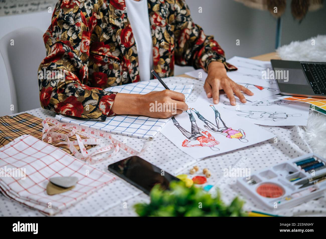 Selektiver Fokus, Nahaufnahme weiblicher Designerin, die Kleidung auf Papier skizziert, Suche nach Ideen für gutes Design mit Laptop-Computern Stockfoto