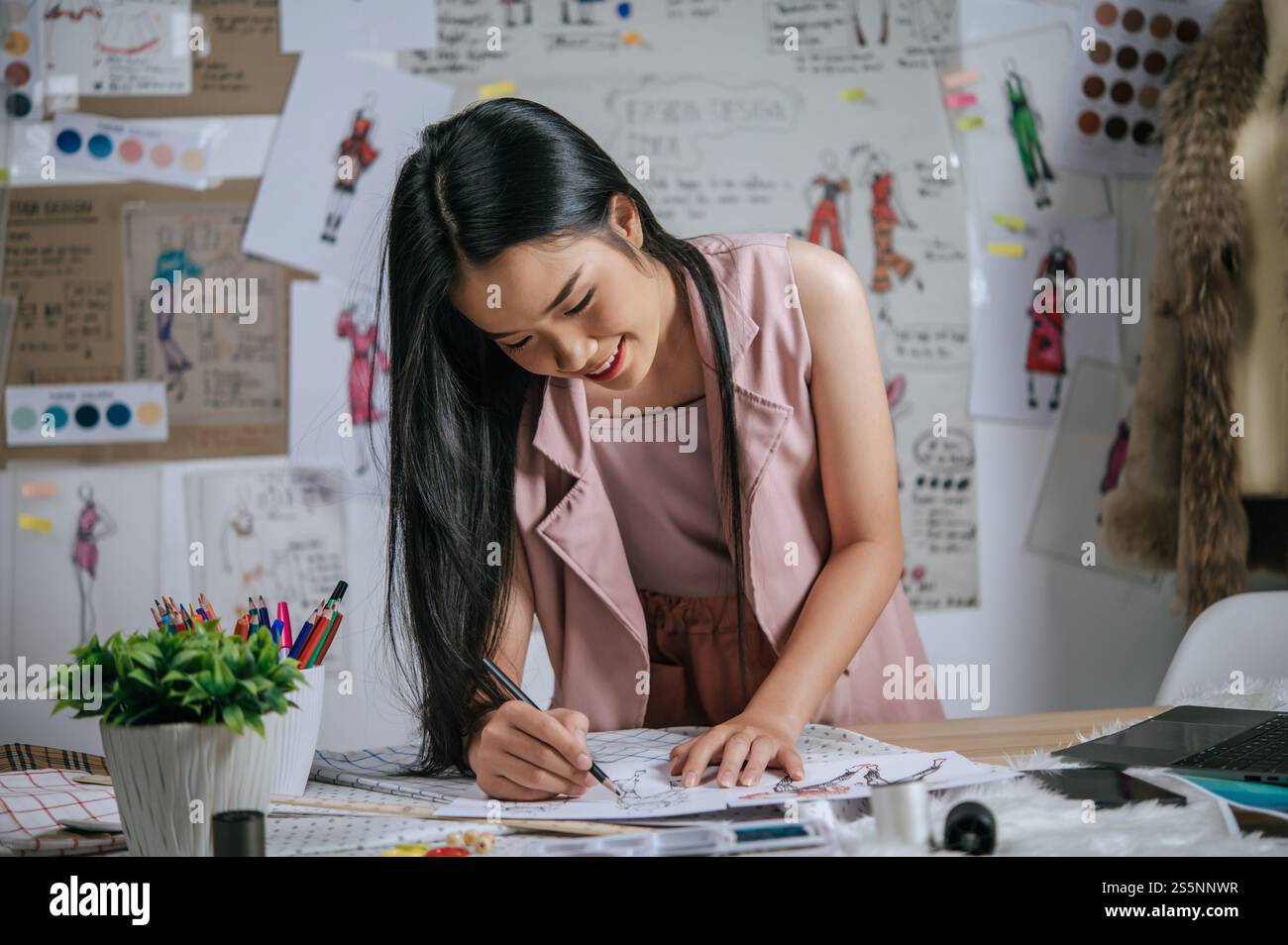 Die junge Designerin steht und skizziert Mode-Kleidung auf Papier, sie lächelt mit Happy Stockfoto