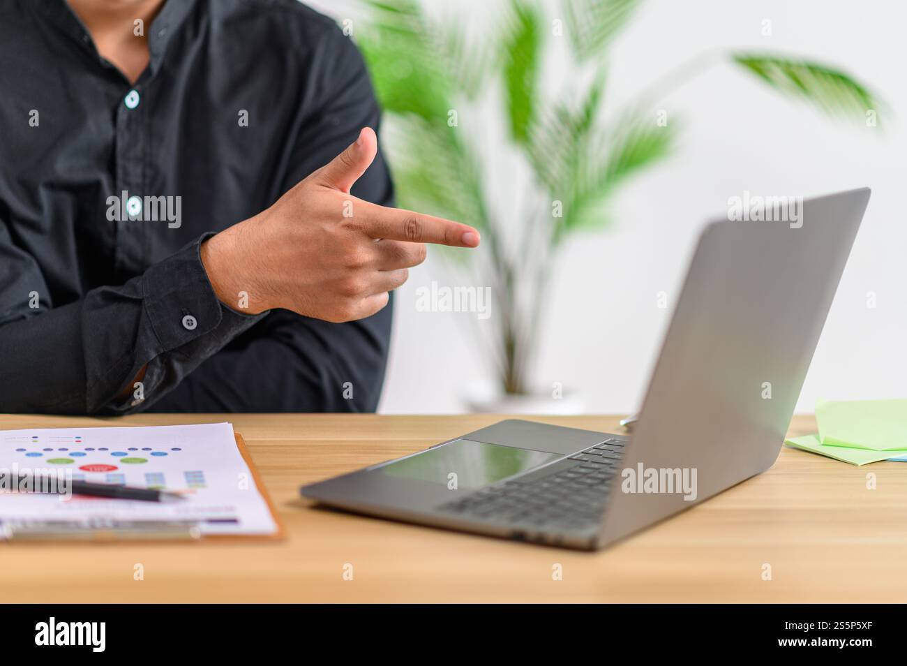 Ein männlicher Arbeiter arbeitet, zeigt auf einen Laptop und hat Dokumente auf dem Tisch. Stockfoto