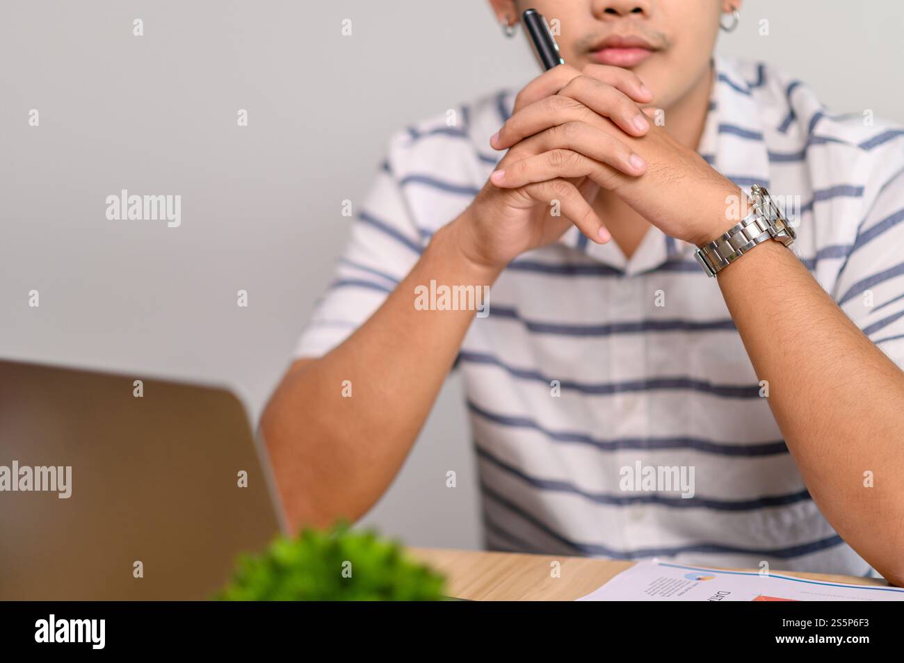 Ein männlicher Arbeiter verwendet einen Laptop mit einer Stiftklemme in der Hand und denkt sich eine Lösung aus. Stockfoto