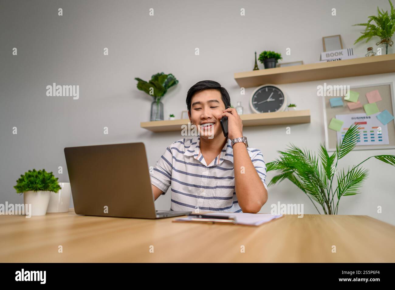 Männlicher Mitarbeiter, der im Büro mit Laptop und Telefon arbeitet Stockfoto