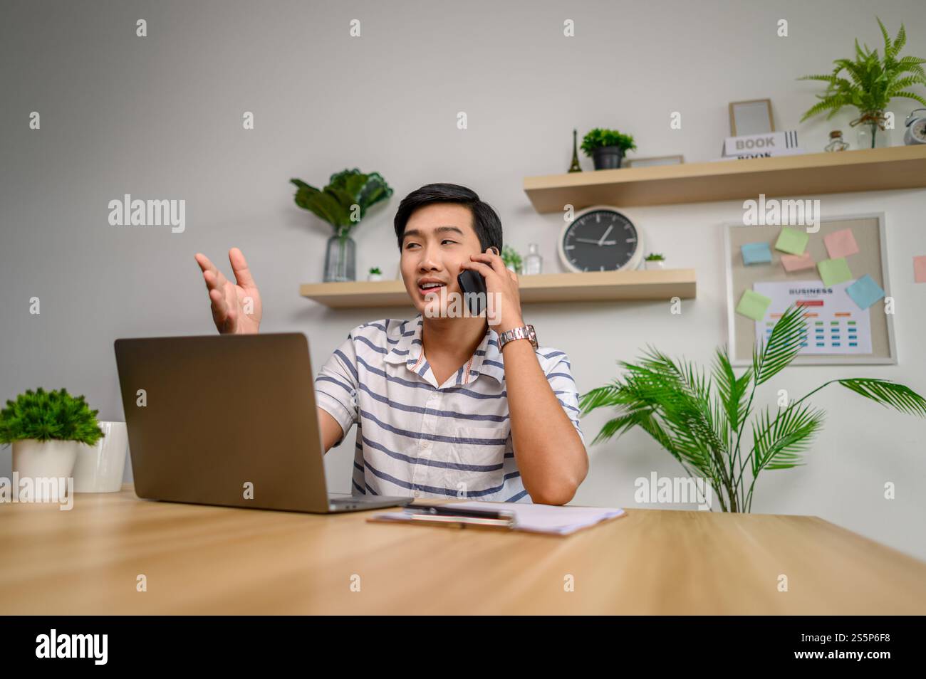 Männlicher Mitarbeiter, der im Büro mit Laptop und Telefon arbeitet Stockfoto