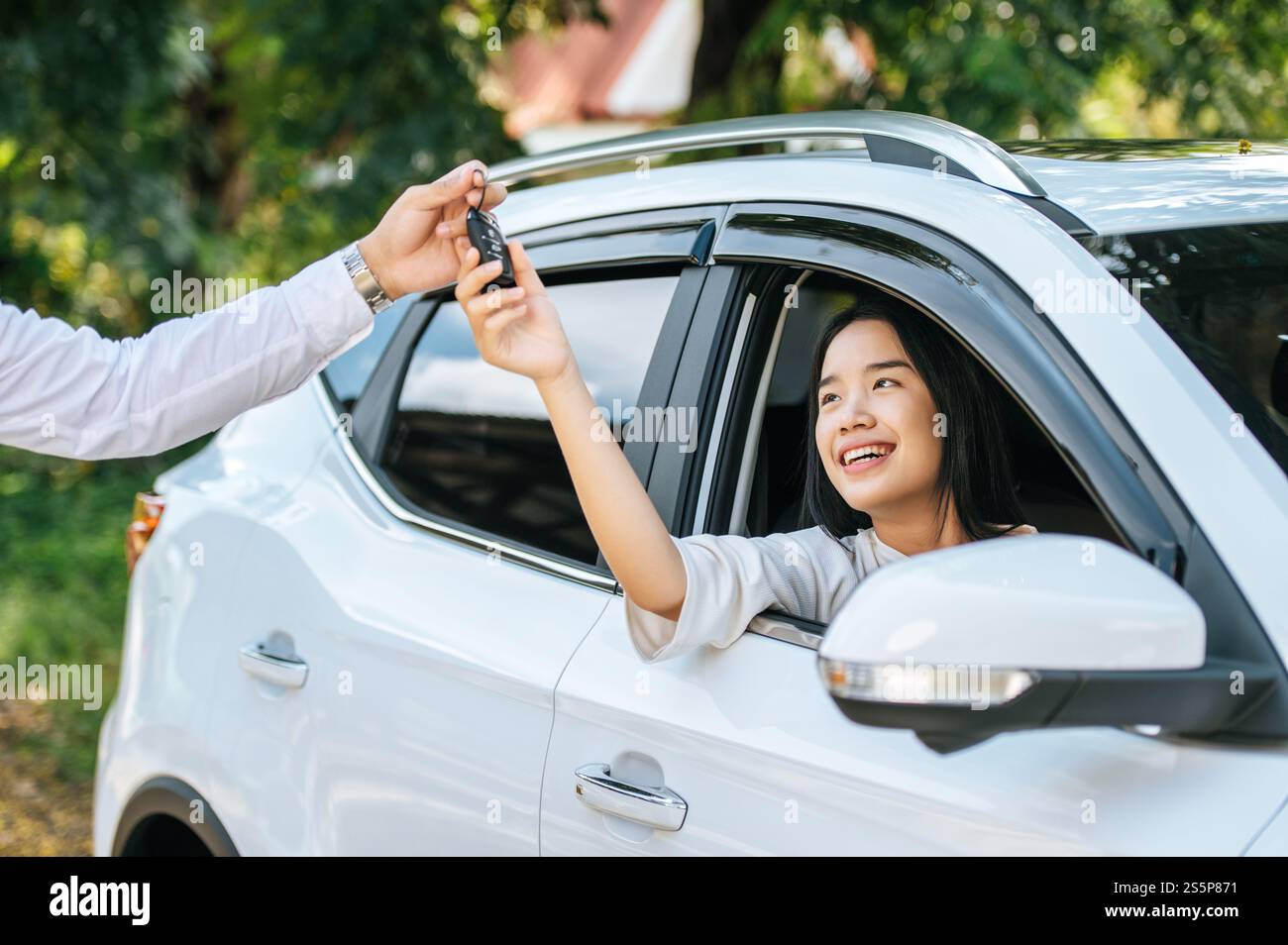 Eine Frau sitzt in einem Auto und hält ihre Hand aus, um die Autoschlüssel zu erhalten. Stockfoto