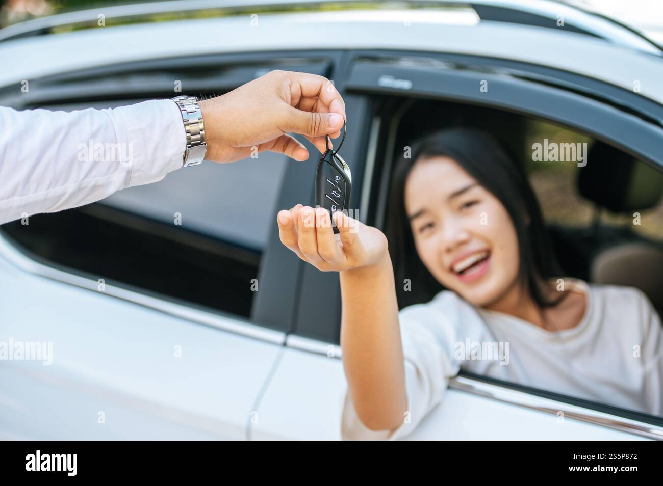 Eine Frau sitzt in einem Auto und hält ihre Hand aus, um die Autoschlüssel zu erhalten. Stockfoto