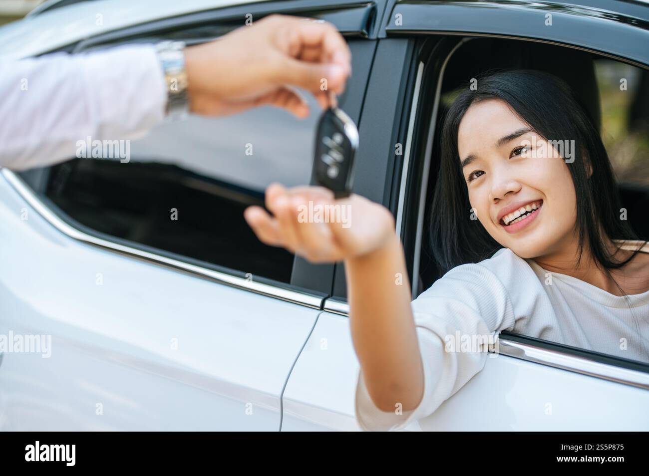 Eine Frau sitzt in einem Auto und hält ihre Hand aus, um die Autoschlüssel zu erhalten. Stockfoto