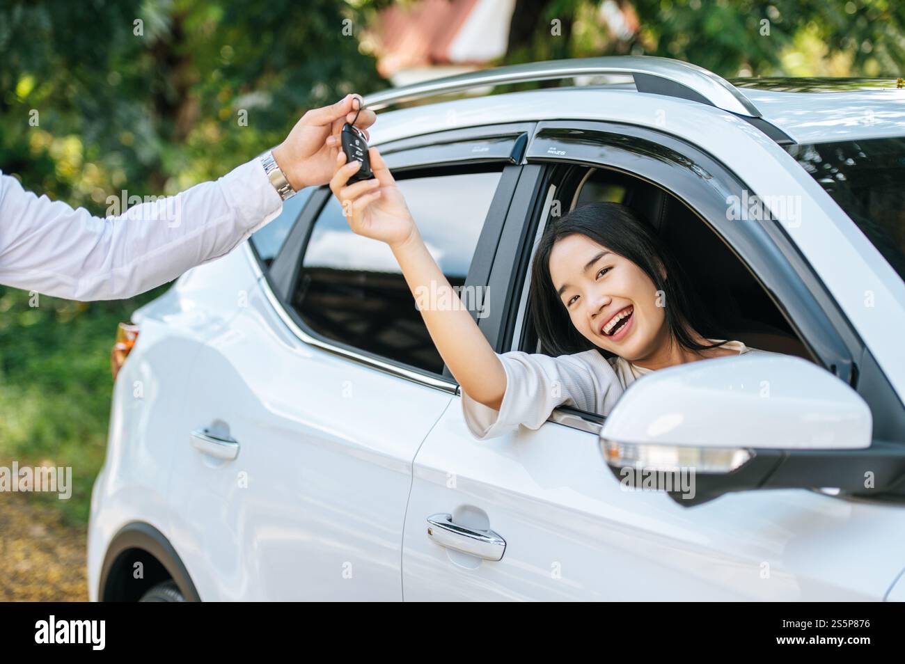 Eine Frau sitzt in einem Auto und hält ihre Hand aus, um die Autoschlüssel zu erhalten. Stockfoto