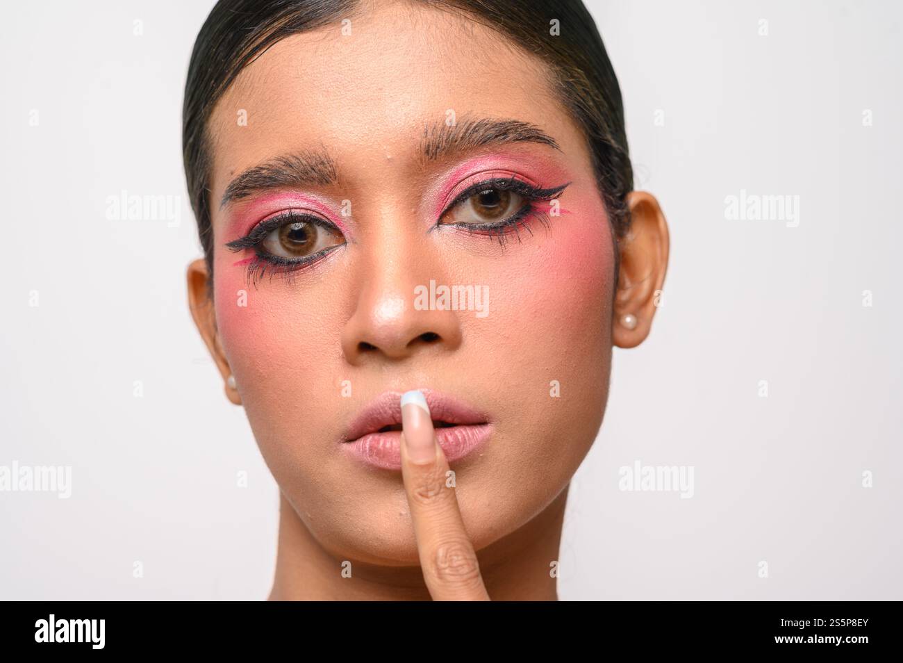 Ein hübsches Mädchen schminkt rosa und legt ihre Finger an den Mund. Isoliert auf weißem Hintergrund Stockfoto