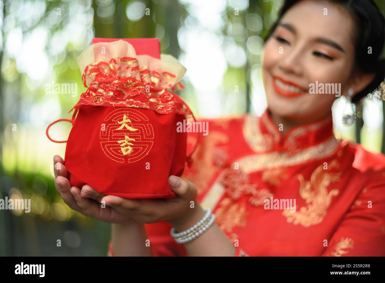 Selektive Fokusumschläge in roter Amuletttasche mit chinesischem Alphabet bedeuten Glück und Glück auf den Händen einer hübschen Frau in chinesischer Kleidung Stockfoto