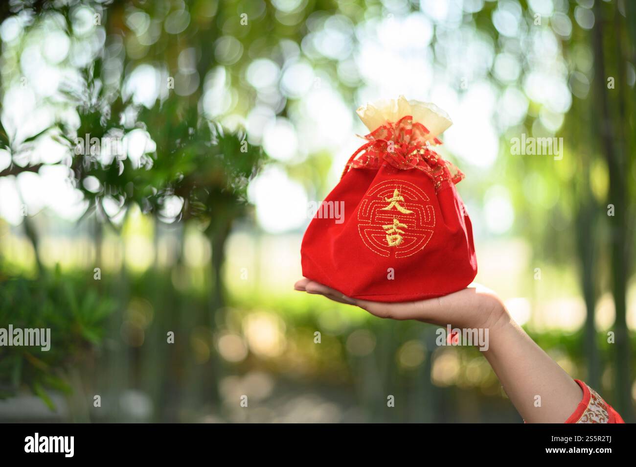 Eine rote Amuletttasche mit chinesischem Alphabet bedeutet Glück und Glück auf weiblicher Hand im Hintergrund des Bambuswaldes, chinesisches Neujahrskonzept, Kopie Stockfoto