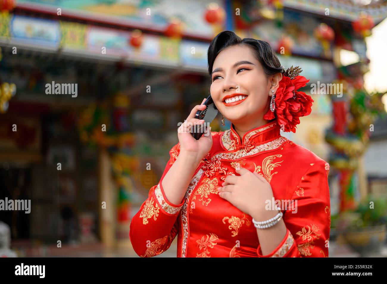 Porträt Asiatische schöne Frau mit einem Cheongsam lächelnd und mit Smartphone am Schrein am chinesischen Neujahr, Kopierraum Stockfoto