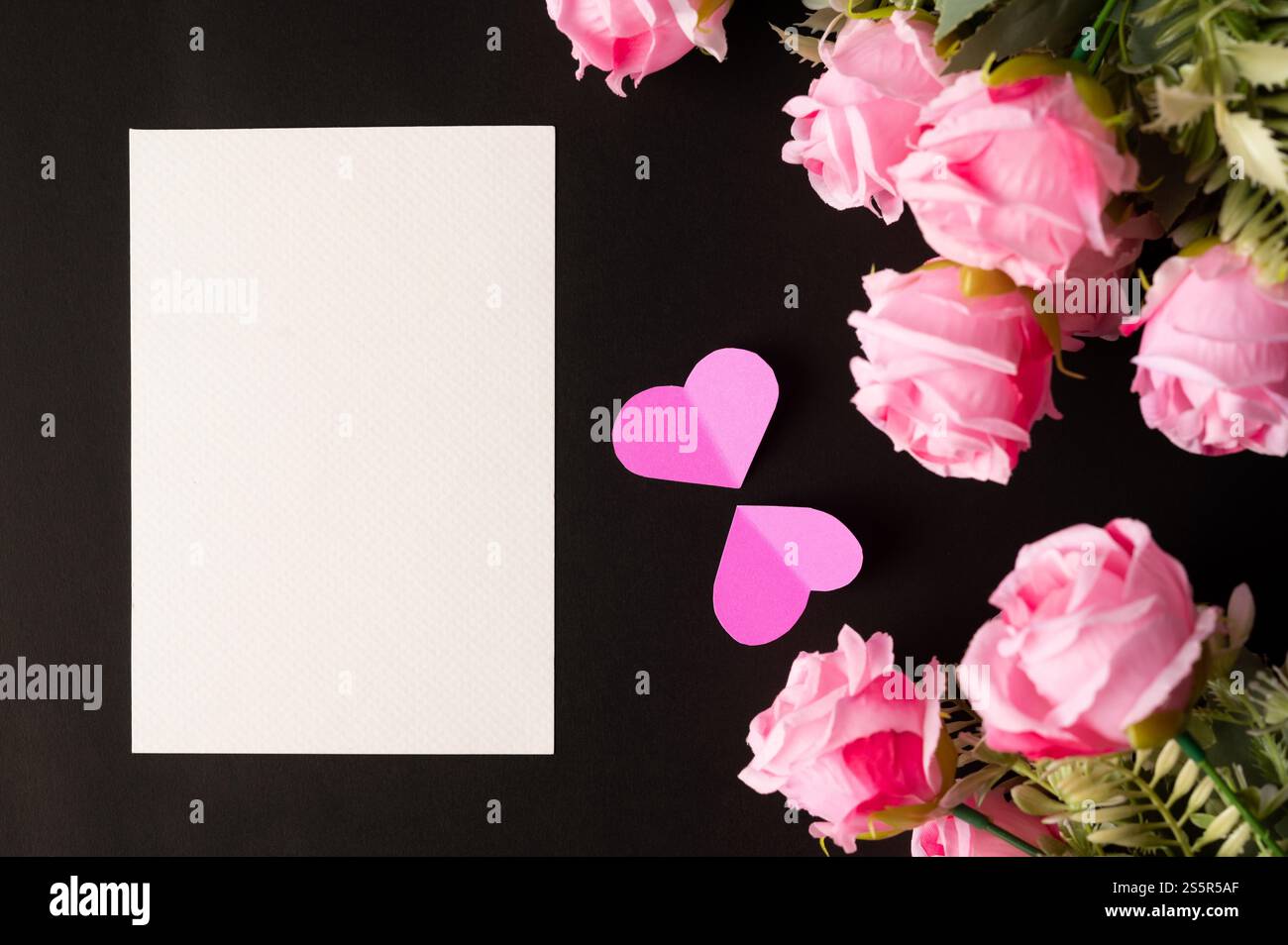 Weißes Papier und rosafarbene Blumen auf schwarzem Hintergrund Stockfoto