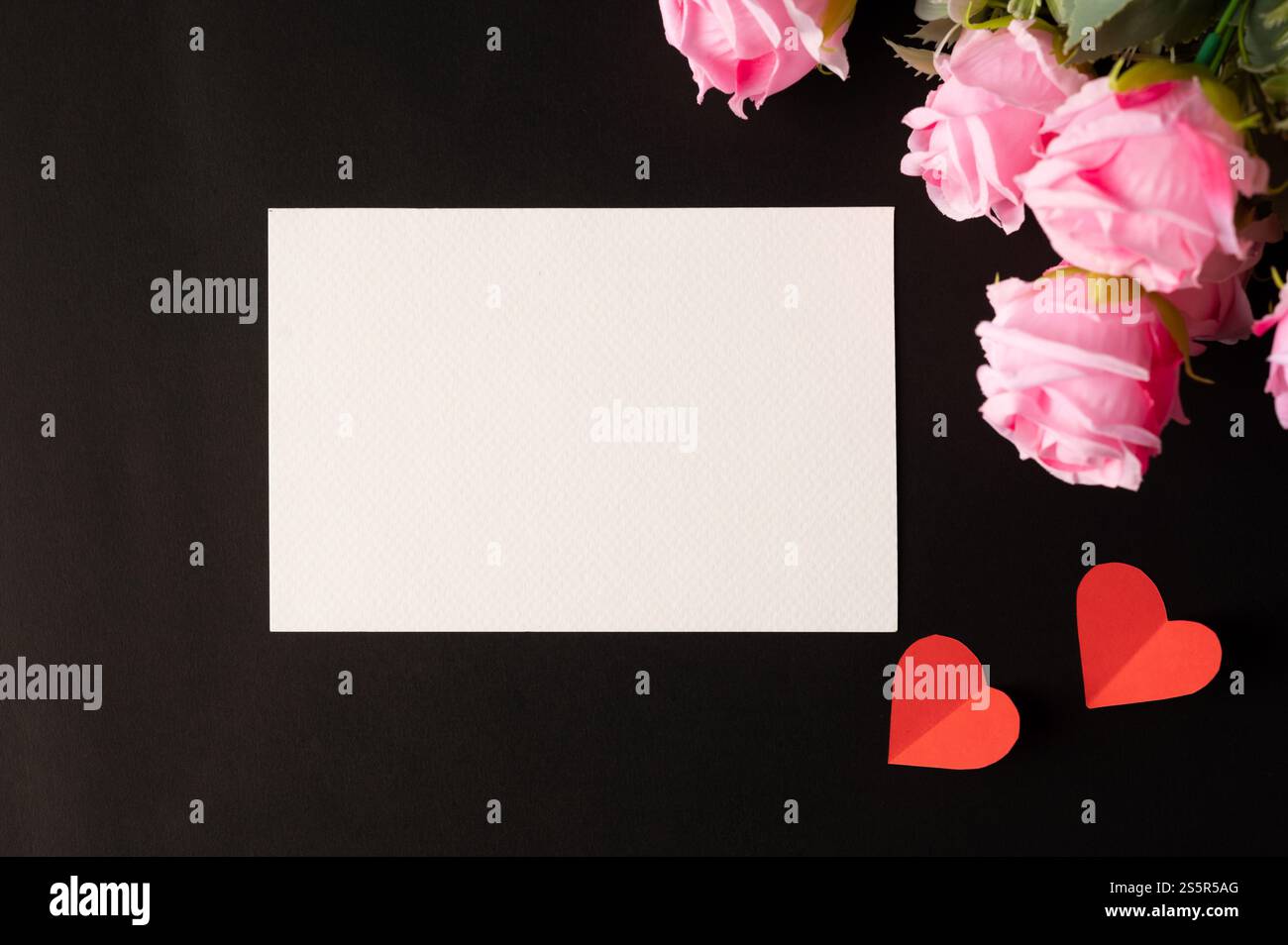 Weißes Papier und rosafarbene Blumen auf schwarzem Hintergrund Stockfoto