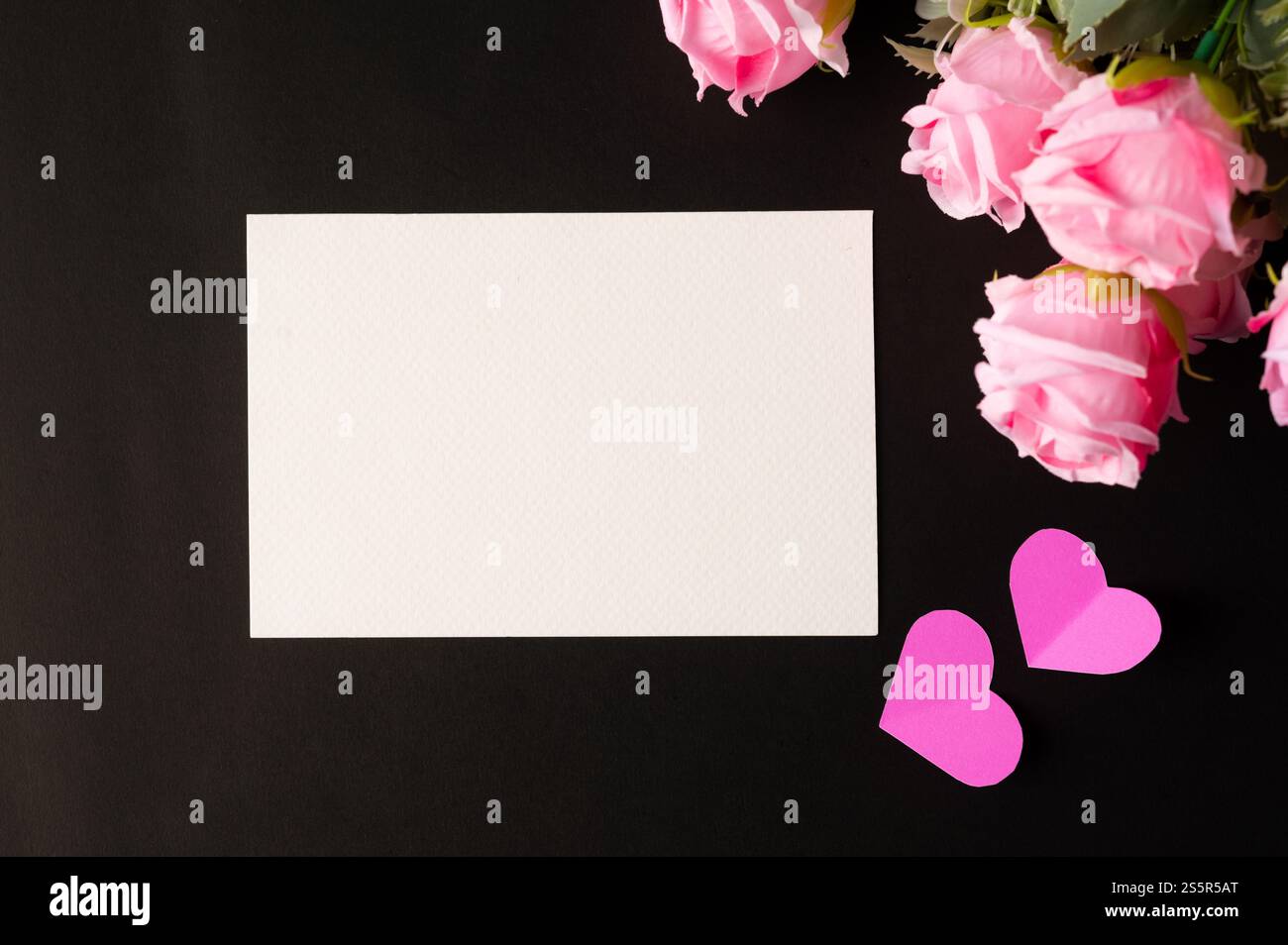 Weißes Papier und rosafarbene Blumen auf schwarzem Hintergrund Stockfoto