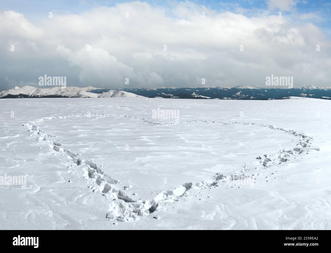 Menschlichen Fußabdruck bilden die Herzform auf schneebedeckten Berg-Plateau und Bergketten hinter. Stockfoto
