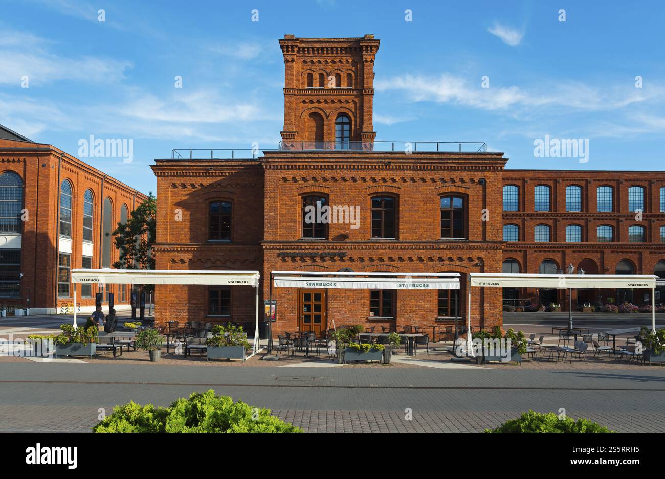 Rotes Backsteingebäude mit Turm und Sitzgelegenheiten im Freien unter klarem Himmel, Manufaktura, Lodz, Lodz, Lodz, Polen, Europa Stockfoto