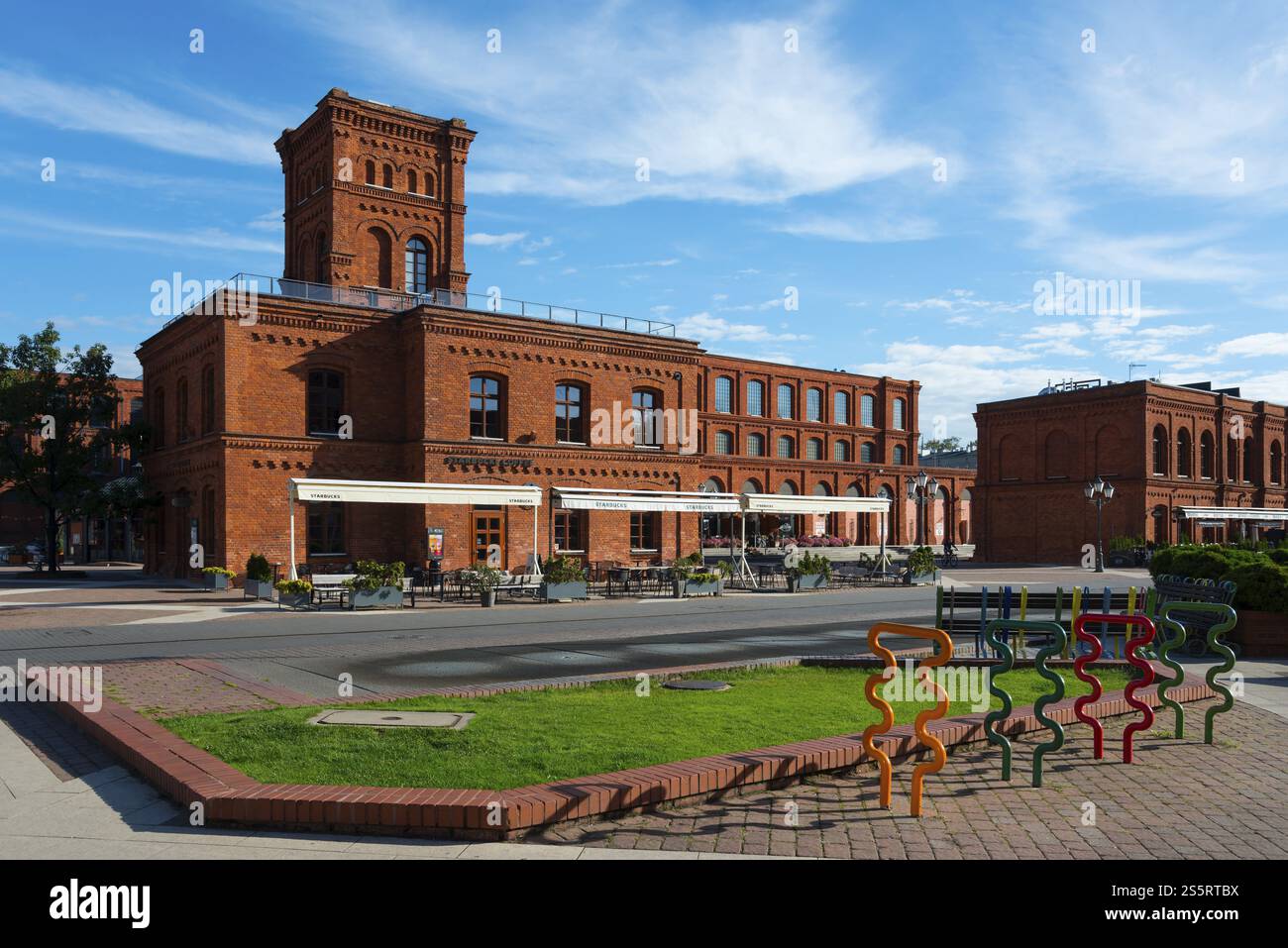Historisches Backsteingebäude mit Sitzbereichen und kleinen Grünflächen unter blauem Himmel, Manufaktura, Lodz, Lodz, Lodz, Polen, Europa Stockfoto