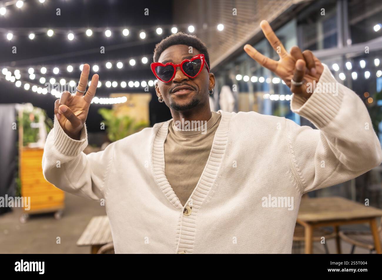 Cooler afrikanischer Mann mit Gesten, der Erfolg beim Lächeln in die Kamera in einer Bar-Terrasse nachts Stockfoto