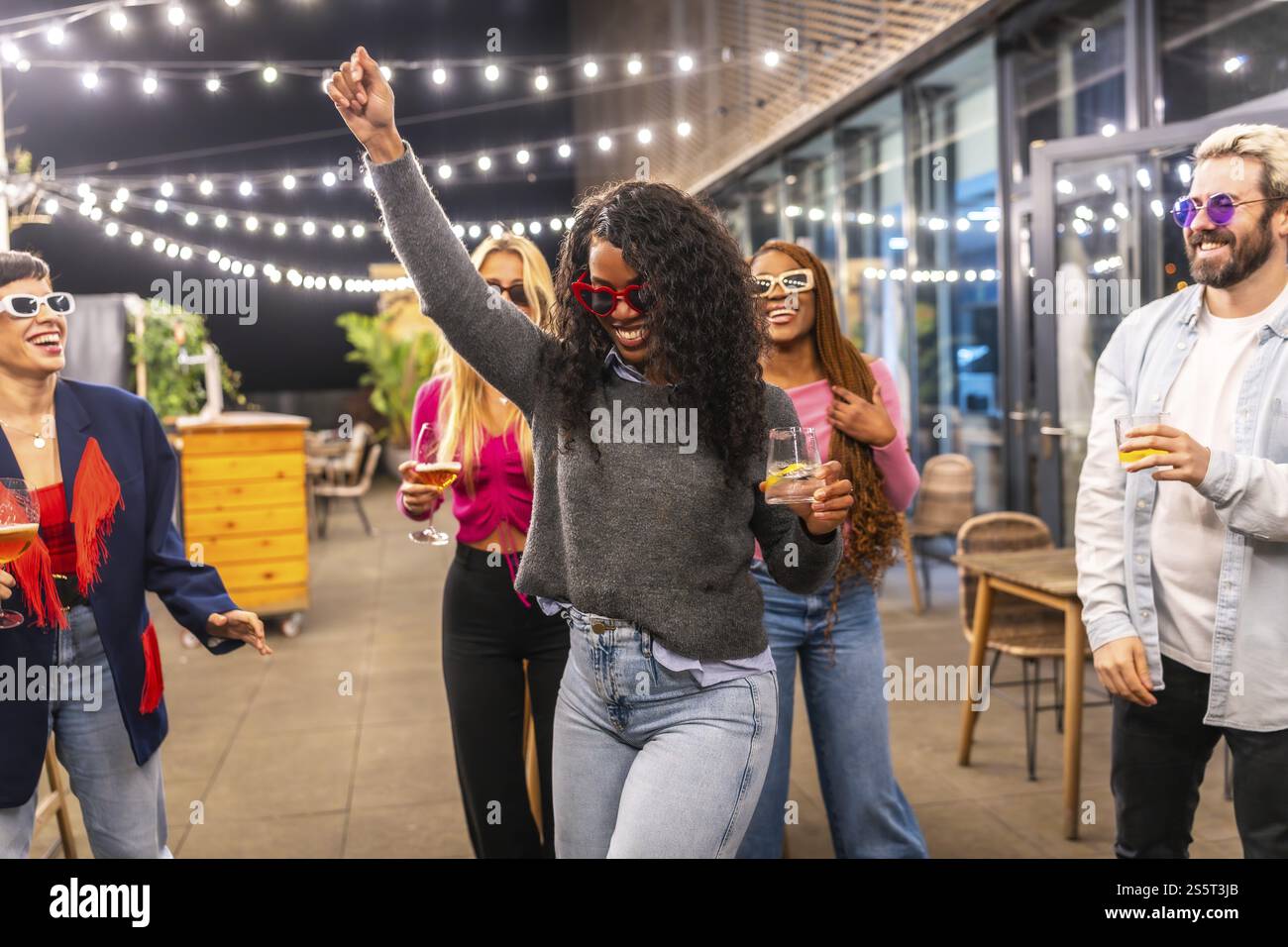 Lateinische Frau, die abends mit Freunden auf der Terrasse einer modernen Stadtbar tanzt Stockfoto