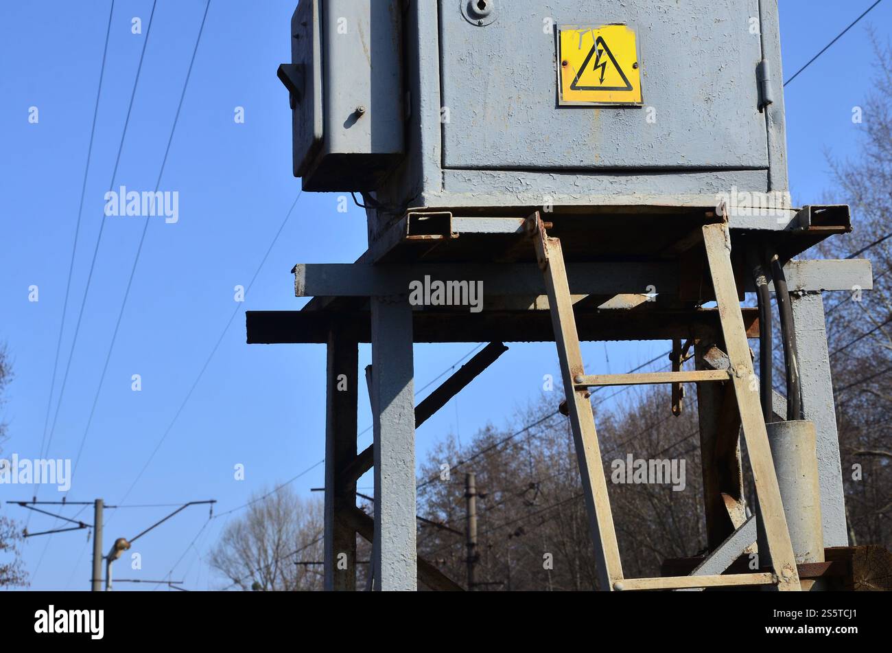 Elektrischer Transformator in Grau mit Symbol zur Warnung vor Hochspannungsgefahr in der Nähe der Eisenbahnstrecke. Eine kleine Umspannstation für die Versorgung von Stockfoto