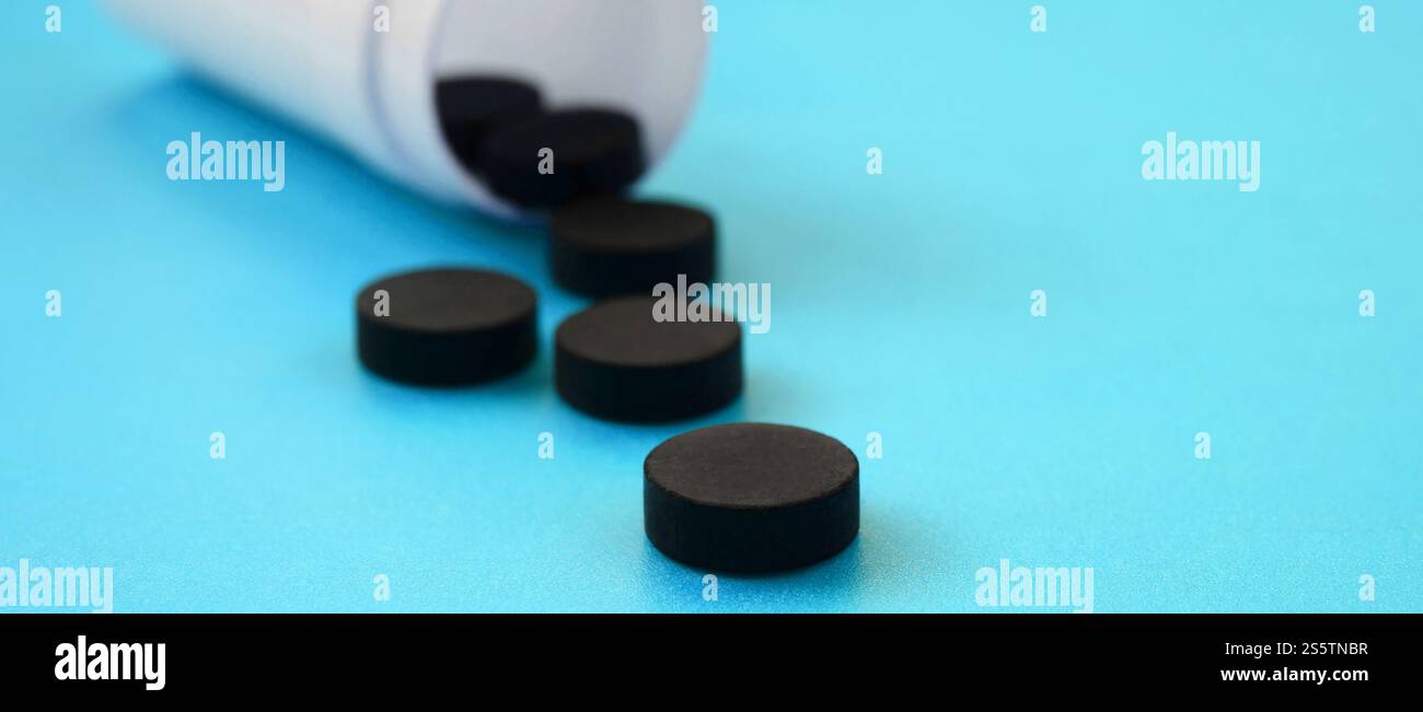 Mehrere schwarze Tabletten fallen aus der Kunststoffbehälter auf der blauen Fläche. Hintergrundbild über medizinische und pharmazeutische Themen. Aktivkohle Stockfoto
