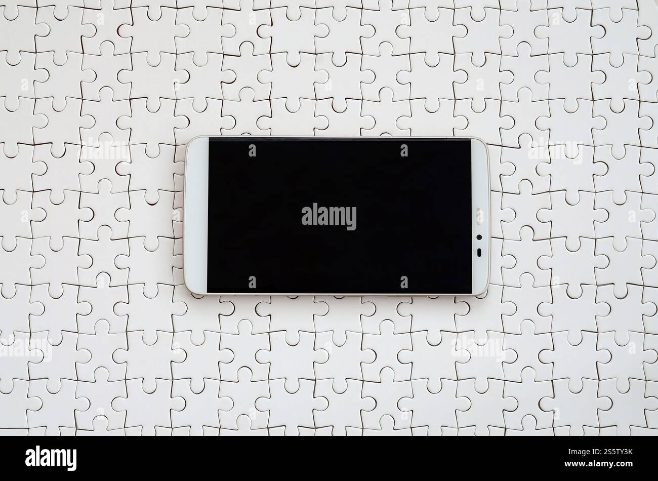 Eine moderne grosse Smartphone mit Touchscreen liegt auf einem weißen Puzzle im zusammengebauten Zustand Stockfoto