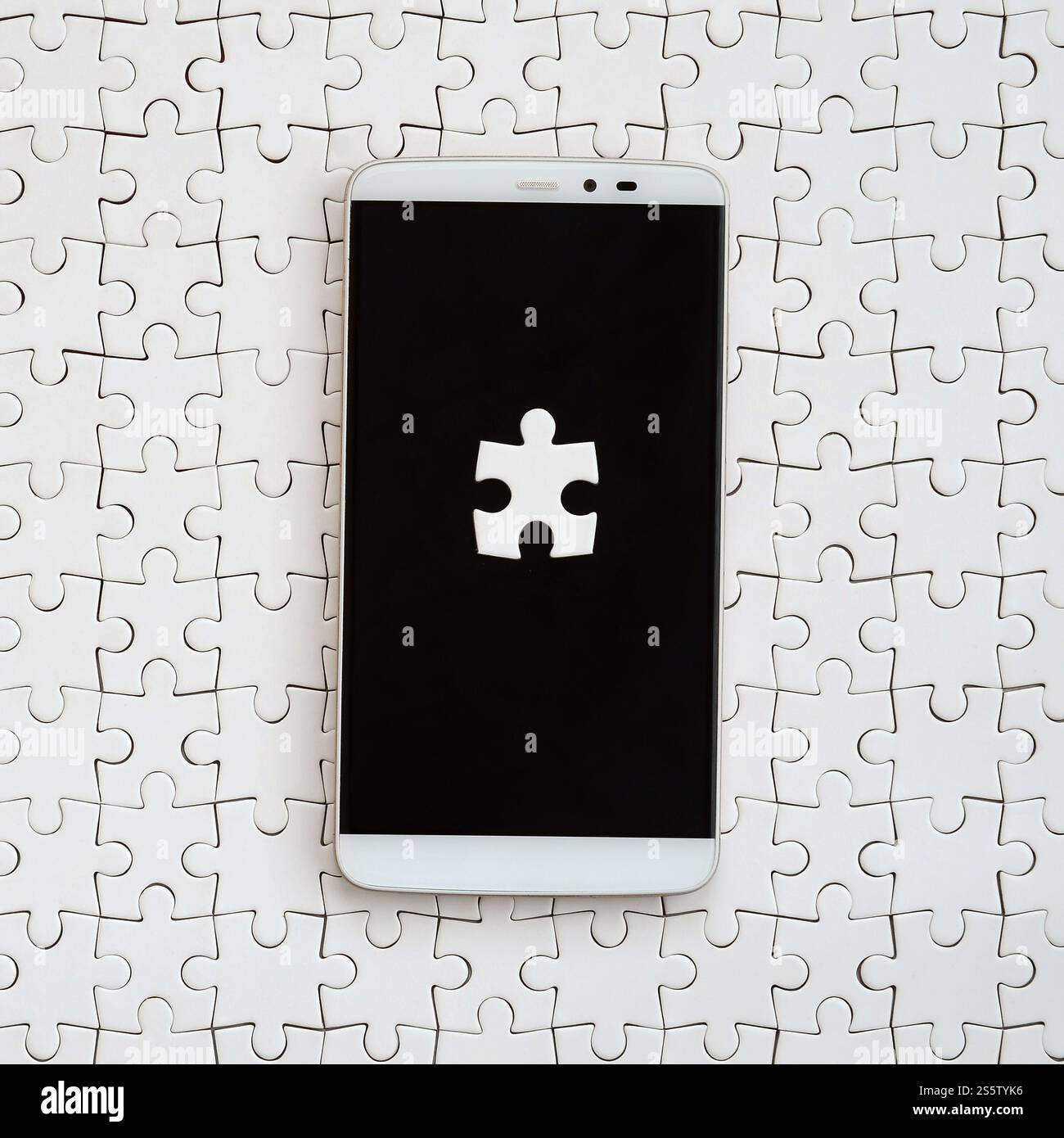 Eine moderne grosse Smartphone mit mehreren puzzle Elemente auf dem Touchscreen liegt auf einem weißen Puzzle im zusammengebauten Zustand Stockfoto