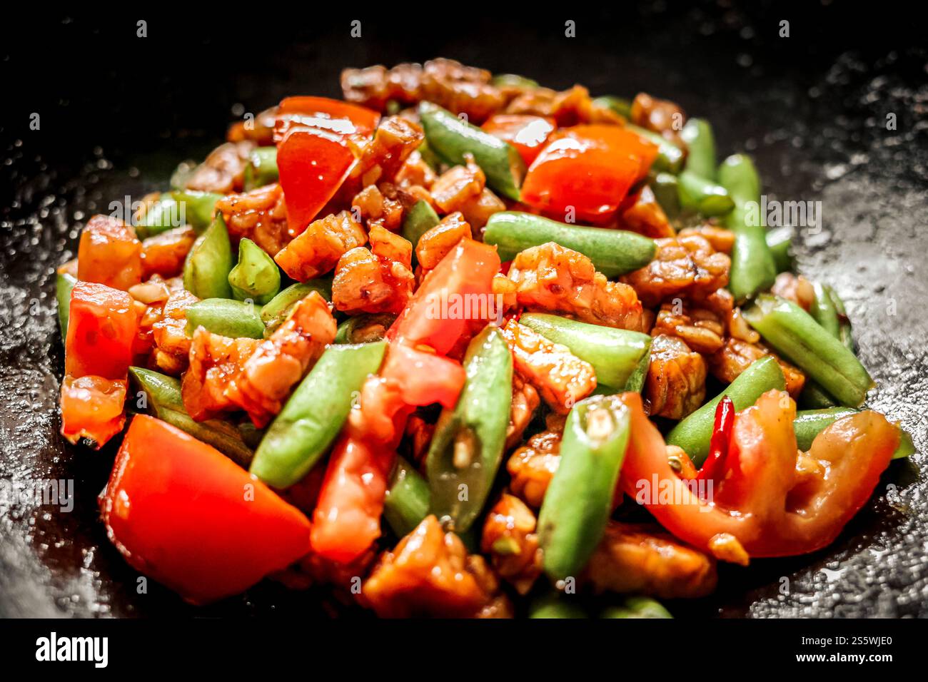 Nahaufnahme der köstlichen indonesischen Speisekarte mit Tempeh und Bohnen mit Tomatenscheiben, die auf einer Pfanne gebraten werden Stockfoto