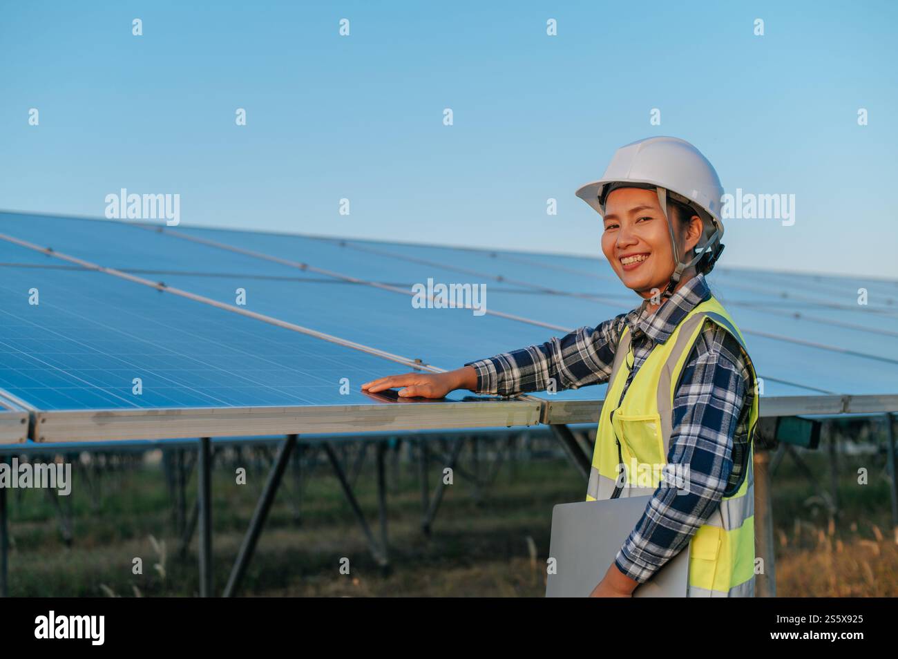 Junge asiatische Inspektorin, die auf die Überprüfung der Operation Photovoltaik-Sonnenkollektor in der Außenstation, hält Laptop-Computer und sucht Stockfoto